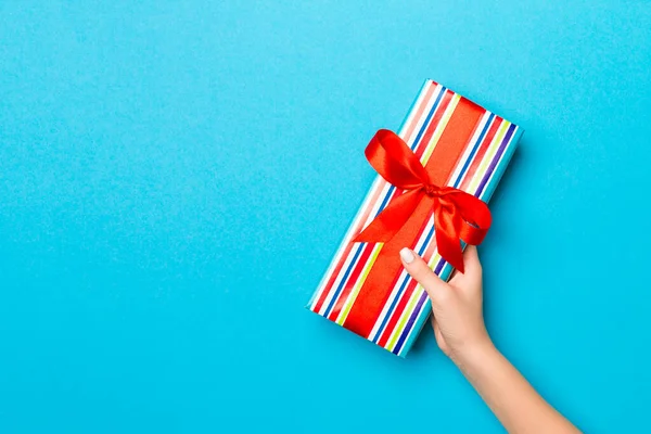 Brazos de mujer sosteniendo caja de regalo con cinta de color en ba mesa azul —  Fotos de Stock