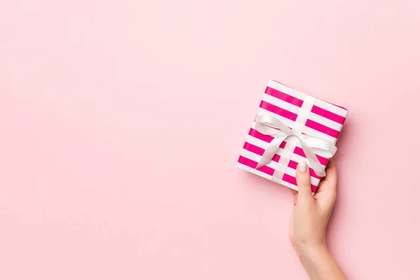 Female's hands holding striped gift box with colored ribbon on l