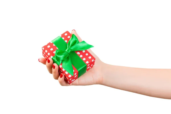 女性の手は緑のリボンで赤い紙に包まれたクリスマスや他の休日の手作りプレゼントを与える。白い背景に、上部のビューに隔離された。感謝祭のギフトボックスコンセプト — ストック写真