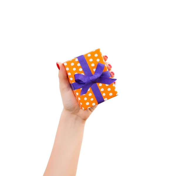 Vrouw handen geven verpakt Kerstmis of andere vakantie met de hand gemaakt in oranje papier met paars lint. Geïsoleerd op witte achtergrond, bovenaanzicht. dankzegging Geschenkdoos concept — Stockfoto