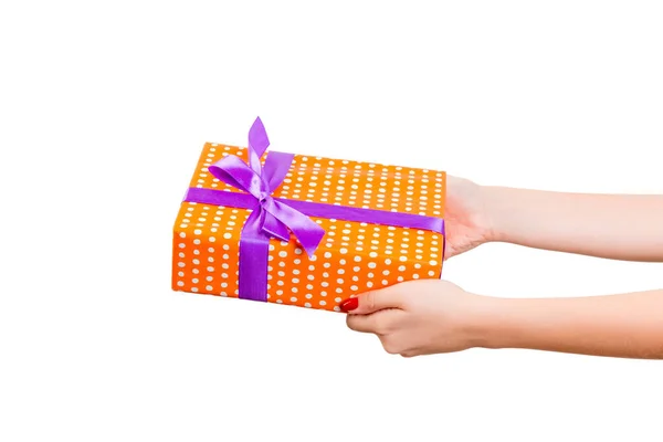 Vrouw handen geven verpakt Kerstmis of andere vakantie met de hand gemaakt in oranje papier met paars lint. Geïsoleerd op witte achtergrond, bovenaanzicht. dankzegging Geschenkdoos concept — Stockfoto