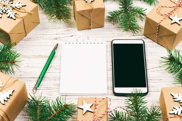 Christmas to do list. Smartphone, noteboock, gift box with red ribbon, shopping list with copy space on white wooden table. Winter holiday concept. Top view. Toned