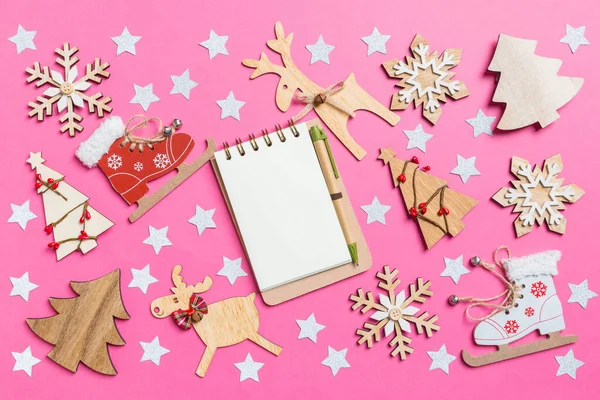 Top view of notebook, pink background decorated with festive toys and Christmas symbols reindeers and New Year trees. Holiday concept — Stock Photo, Image