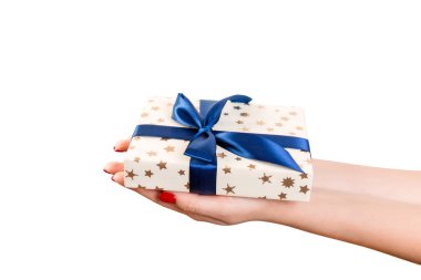 Kadın elleri, mavi kurdeleli altın kağıda sarılı Noel ya da diğer tatil hediyelerini verir. Beyaz arkaplanda izole edilmiş, üst manzara. Şükran Günü hediye kutusu konsepti