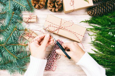 Noel dekoruyla ahşap arka planda el yapımı bir hediye. Kadın Noel hediyesini paketliyor, Noel hediyelerini çam ağacı ve çam kozalağıyla hazırlıyor. Üst görünüm, boşluğu kopyala. Ayarlanmış
