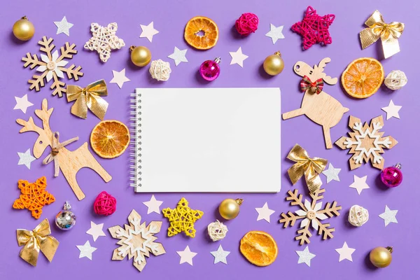 Bovenaanzicht van notebook omgeven met Nieuwjaar speelgoed en decoraties op paarse achtergrond. Kerstconcept — Stockfoto