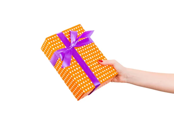 Vrouw handen geven verpakt Kerstmis of andere vakantie met de hand gemaakt in oranje papier met paars lint. Geïsoleerd op witte achtergrond, bovenaanzicht. dankzegging Geschenkdoos concept — Stockfoto