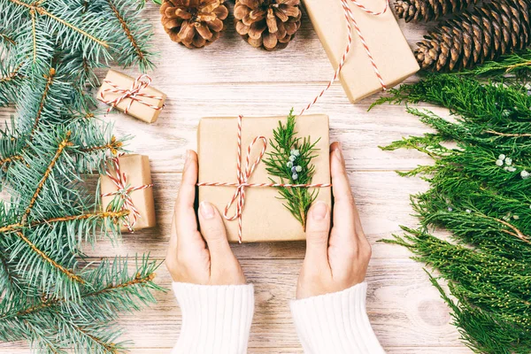 Met de hand gemaakt cadeau op houten achtergrond met kerstdecor. Vrouw inpakken kerstcadeau, meisje bereidt kerstcadeaus met dennenboom en dennenappel. Bovenaanzicht, kopieer ruimte. Getooid — Stockfoto