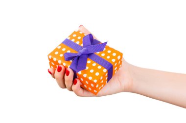 Kadın elleri, paketlenmiş Noel ya da diğer tatil hediyelerini mor kurdeleli turuncu kağıda sarar. Beyaz arkaplanda izole edilmiş, üst manzara. Şükran Günü hediye kutusu konsepti