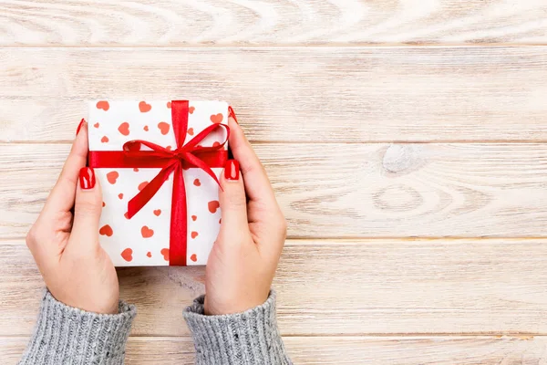 Les mains de femme donnent valentin enveloppé ou autre cadeau fait à la main de vacances en papier avec ruban rouge. Boîte cadeau, décoration coeur rouge de cadeau sur table en bois, vue du dessus avec espace de copie pour vous la conception — Photo