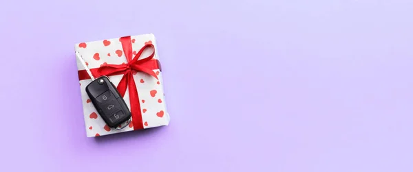 Car key on paper gift box with red ribbon bow and heart on violet table background. Holidays present top view concept — Stock Photo, Image
