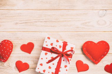 Sevgililer veya diğer tatil el yapımı mevcut kağıt ile tatil sarmalayıcı kırmızı kalpler ve hediye kutusunda. Tasarım için turuncu ahşap masa üstten görünüm kopya alanı ile boş alanı hediye kutusu