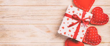 Sevgililer veya diğer tatil el yapımı mevcut kağıt ile tatil sarmalayıcı kırmızı kalpler ve hediye kutusunda. Tasarım için turuncu ahşap masa üstten görünüm kopya alanı ile boş alanı hediye kutusu