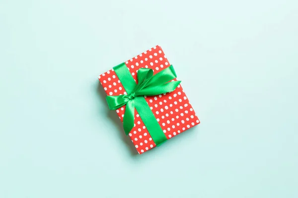 Wrapped Christmas or other holiday handmade present in paper with green ribbon on blue background. Present box, decoration of gift on colored table, top view with copy space — Stock Photo, Image