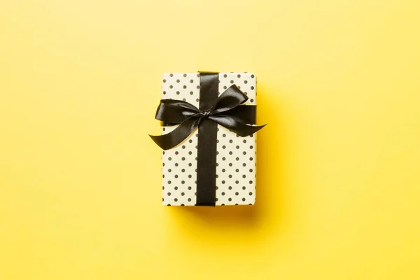 Envuelto Navidad u otro regalo hecho a mano de vacaciones en papel con cinta negra sobre fondo amarillo. Caja de regalo, decoración de regalo en mesa de colores, vista superior con espacio para copiar — Foto de Stock