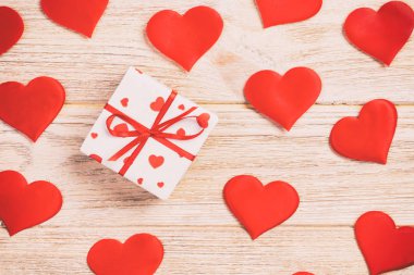 Sevgililer veya diğer tatil el yapımı mevcut kağıt ile tatil sarmalayıcı kırmızı kalpler ve hediye kutusunda. Tasarım için turuncu ahşap masa üstten görünüm kopya alanı ile boş alanı hediye kutusu