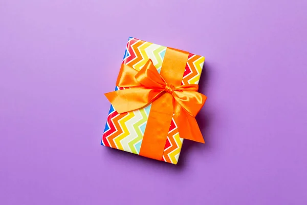 Gift box with orange bow for Christmas or New Year day on purple background, top view with copy space — Stockfoto