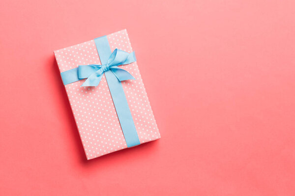 Top view Christmas present box with blue bow on living coral background with copy space