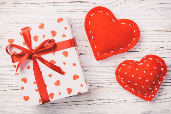 Valentine or other holiday handmade present in paper with red hearts and gifts box in holiday wrapper. Present box of gift on white wooden table top view with copy space, empty space for design — Stock Photo, Image