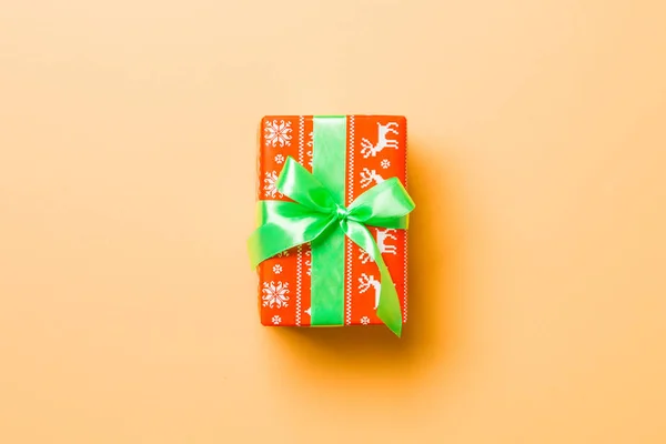 Enveloppé Noël ou autre cadeau de vacances fait à la main en papier avec ruban vert sur fond orange. Coffret cadeau, décoration de cadeau sur table colorée, vue de dessus avec espace de copie — Photo