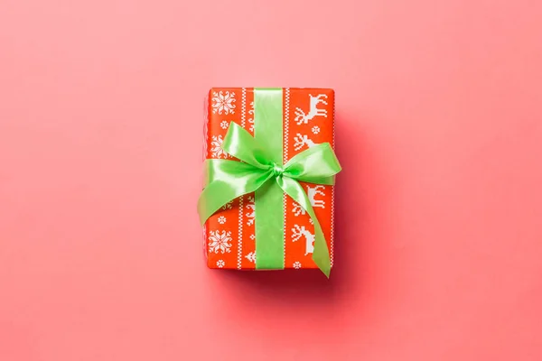 Verpackte Weihnachten oder andere Feiertage handgemachtes Geschenk in Papier mit grünem Band auf lebendigem Korallenhintergrund. Geschenkbox, Geschenkdekoration auf farbigem Tisch, Draufsicht mit Kopierraum — Stockfoto