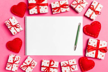 Renkli arka planda hediye kutuları ve kalplerle çevrili defterin üst görüntüsü. Sevgililer Günü konsepti