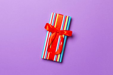 Noel 'i ya da diğer tatil hediyelerini mor arka planda kırmızı kurdeleli kağıda sardım. Şimdiki kutu, renkli tabloda hediye süslemesi, kopya alanı ile üst görünüm