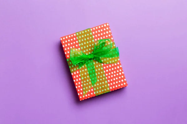 Zabalené vánoční nebo jiné sváteční ručně vyráběné dárek v papíru se zelenou stuhou na fialovém pozadí. Dárek box, dekorace dárku na barevném stole, horní pohled s kopírovacím prostorem — Stock fotografie