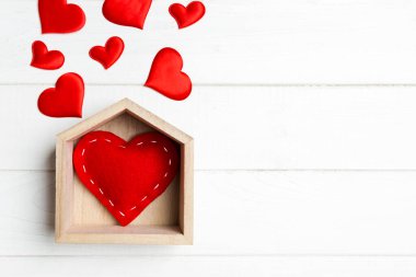 Ahşap arka planda küçük kalplerle çevrili bir evde kırmızı kalpten yapılmış üst görünüm. Evim güzel evim konsepti. Sevgililer Günü