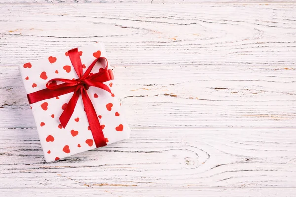 Valentine or other holiday handmade present in paper with red hearts and gifts box in holiday wrapper. Present box of gift on white wooden table top view with copy space, empty space for design — Stock Photo, Image