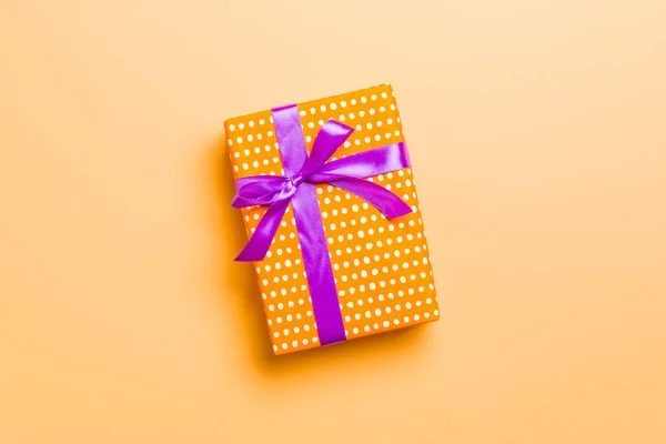 Avvolto Natale o altra vacanza fatto a mano presente in carta con nastro viola su sfondo arancione. Scatola regalo, decorazione del regalo sulla tavola colorata, vista dall'alto con spazio di copia — Foto Stock