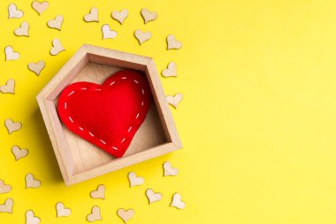 Renkli arka planda küçük kalplerle süslenmiş ahşap bir evde kırmızı tekstil kalbinin en üst görüntüsü. Kalbin şekli. Evim güzel evim. Sevgililer Günü konsepti