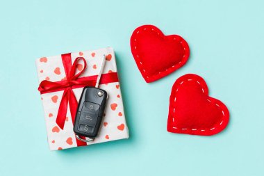 Hediye kutusundaki araba anahtarının üst görüntüsü ve renkli arka plandaki kırmızı tekstil kalpleri. Sevgililer Günü konsepti için hediye