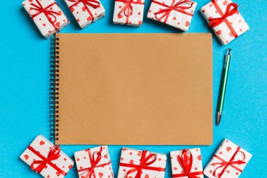 Renkli arka planda hediye kutularıyla çevrili el sanatları defterinin üst görüntüsü. Sevgililer Günü