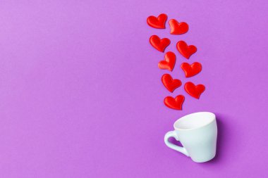 Kırmızı kalplerin üst görünüm kompozisyonu fotokopi alanı ile renkli arkaplandaki bir bardaktan dökülüyor. Romantik ilişki kavramı. Aziz Valentaine Günü