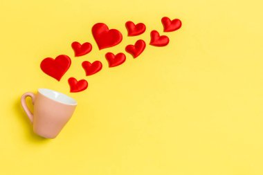 Kırmızı tekstil kalplerinin renkli arka planda bir bardaktan fışkırması. Sevgililer günün kutlu olsun.