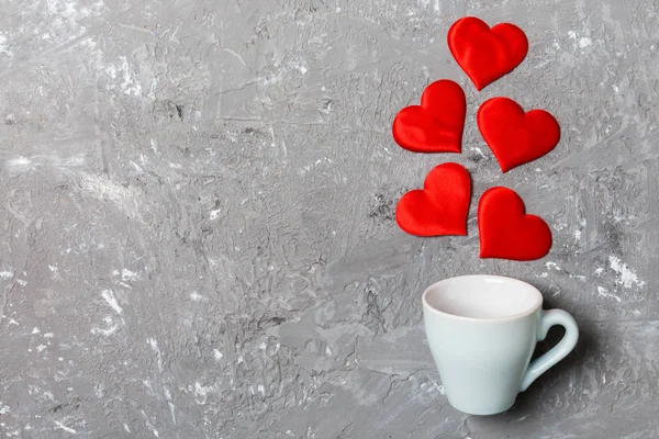 Top view of a cup and red hearts falling out from it on cement background. Happy Valentine's Day concept