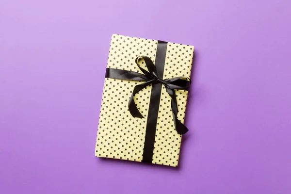 Gift box with black bow for Christmas or New Year day on purple background, top view with copy space — Stock Photo, Image