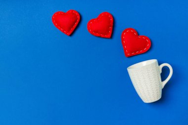 Kırmızı tekstil kalplerinin renkli arka planda bir bardaktan fışkırması. Sevgililer günün kutlu olsun.
