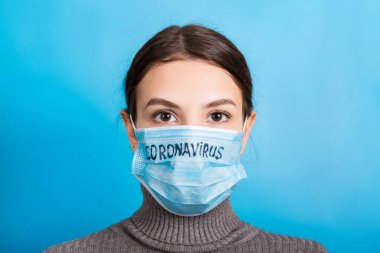 Mavi arka planda Coronavirus metni olan tıbbi maskeli bir kadının portresi. Coronavirus konsepti. Solunum koruması