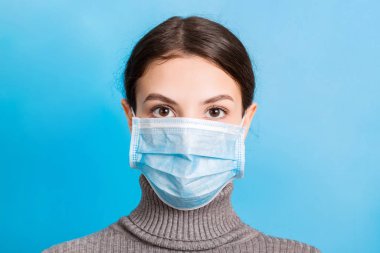 Mavi arka planda tıbbi maske takan genç bir kadının portresi. Sağlığınızı koruyun. Coronavirus konsepti