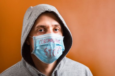 Korunaklı tıbbi maske takan kapüşonlu bir gencin portresi. Kahverengi arka planda Coronavirus metnini durdurmuş. Coronavirus konsepti. Sağlık hizmetleri kavramı