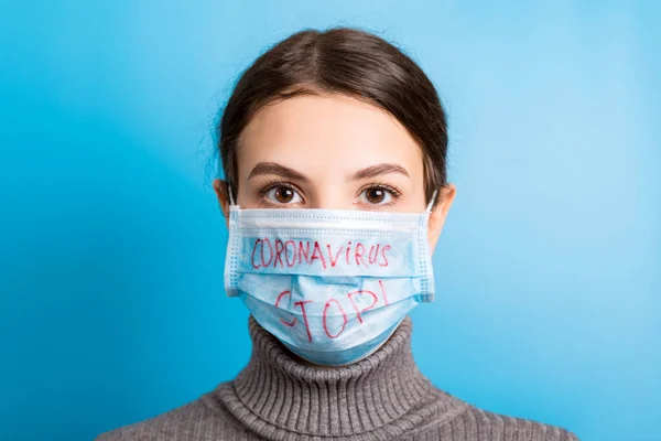 Portretul unei femei în mască medicală cu text stop coronavirus pe fundal albastru. Conceptul de coronavirus. Protecție respiratorie — Fotografie, imagine de stoc