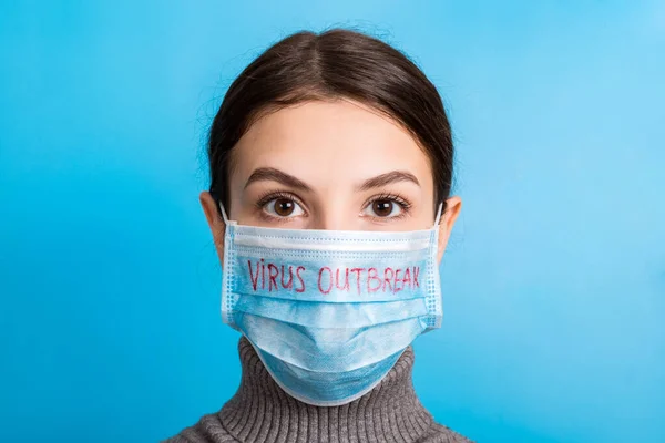 Portretul unei femei drăguțe care poartă mască medicală cu text focar de virus pe fundal albastru. Conceptul de coronavirus. Protecție respiratorie — Fotografie, imagine de stoc