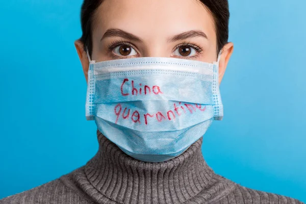 Muotokuva naisesta, jolla on lääketieteellinen naamio ja karanteenisana sinisellä pohjalla. Coronavirus ja terveydenhuollon käsite — kuvapankkivalokuva