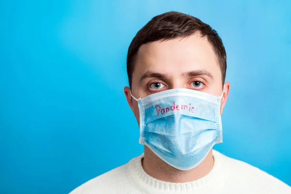 Portrait of young man in protective mask with pandemic text at blue background. Coronavirus and health care concept — 스톡 사진