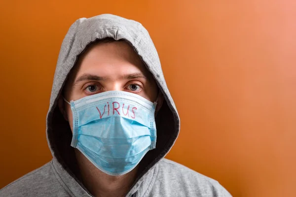 Portrait of a man in hood on his head wearing medical mask with virus word at brown background. Coronavirus concept. Respiratory protection concept — 스톡 사진