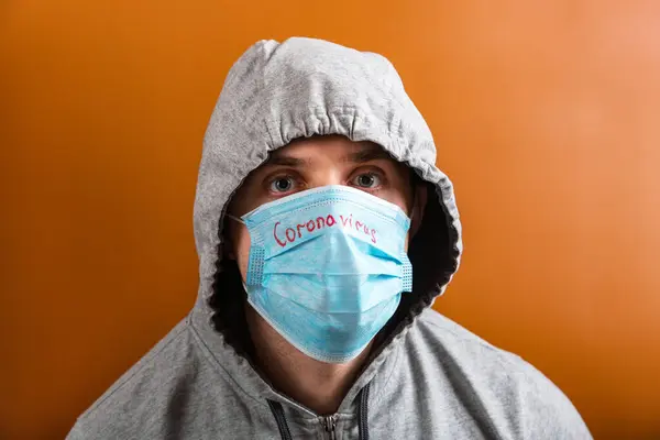 Portrait of a man in hood on his head wearing medical mask with coronavirus word at brown background. Coronavirus concept. Respiratory protection concept — 스톡 사진