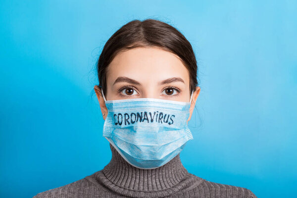 Portrait of a woman in medical mask with coronavirus text at blue background. Coronavirus concept. Respiratory protection Stock Photo