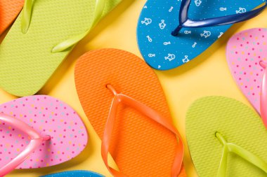 many colored flip flops on yellow background. Copy space top vie